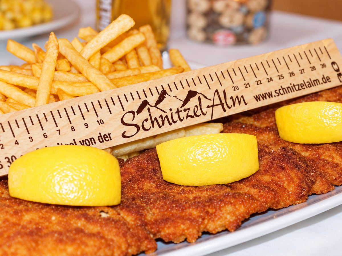Das 30-cm-Schnitzel der Schnitzelalm mit Pommes frites, Zitronen und dem hölzernen Lineal